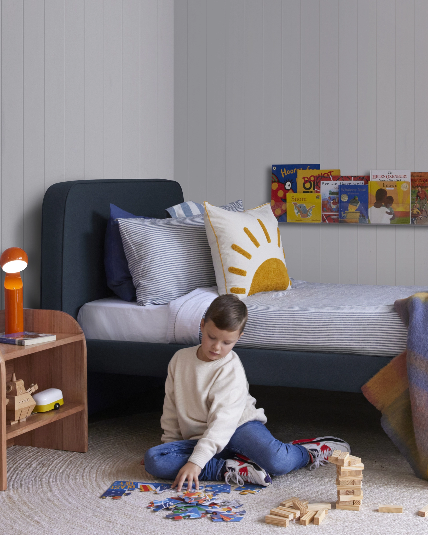 Child playing with toys on the floor in a bedroom with a blue fabric bed and books in the background.