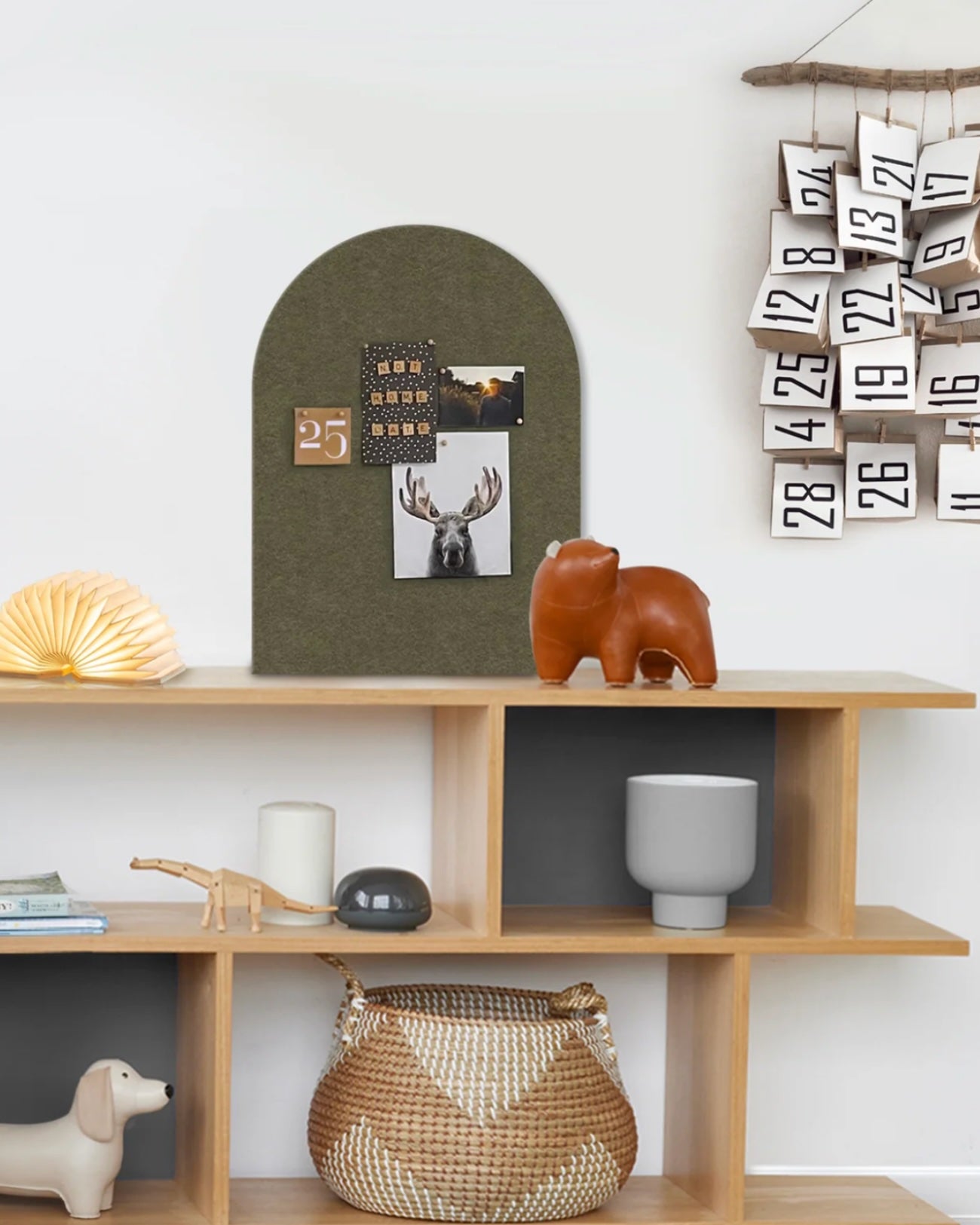 Wooden bookcase with decorative items including an felt arch pinboard, to help organise the home. The bookcase features a small bear figurine, and a calendar on a white wall.