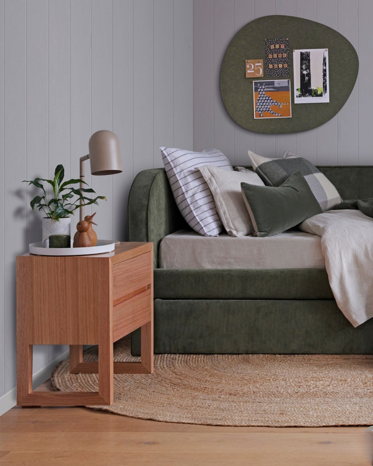 Olive-coloured daybed with modern curved design and matching trundle bed. Features timber bedside table and felt pinboard in a pebble shape on the wall.