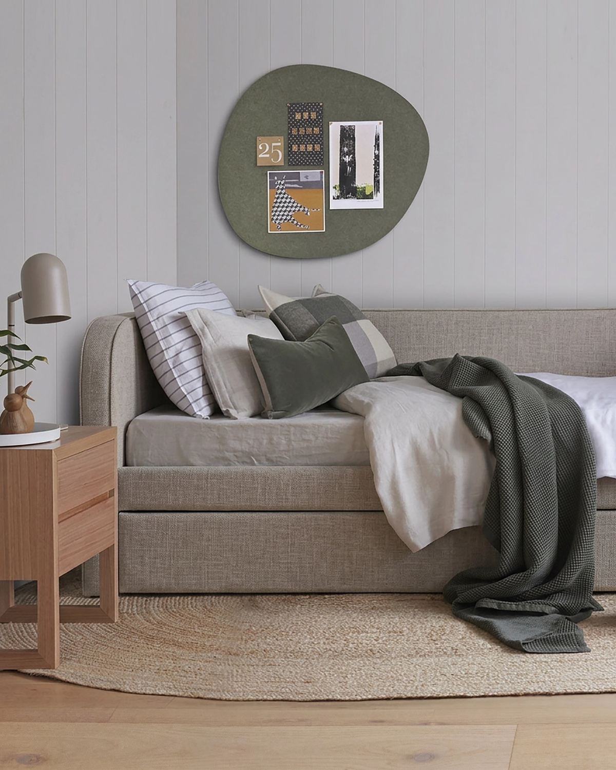 Pebble shaped felt pinboard in olive colour on a bedroom wall, with art prints pinned to its curved organic form.