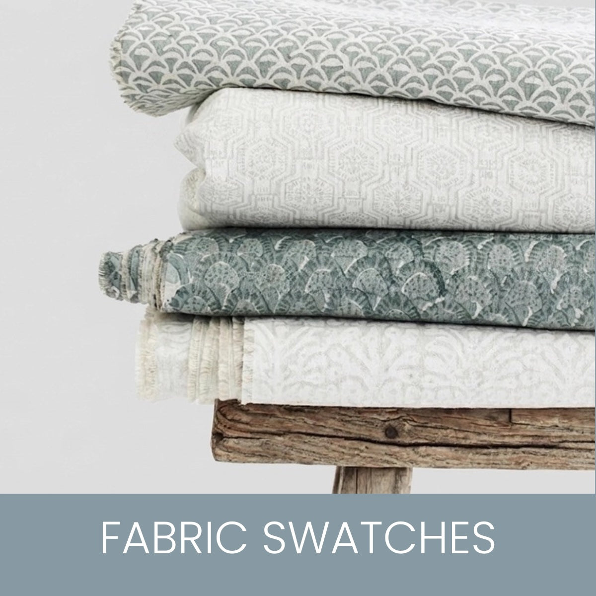 Four folded fabric samples stacked on a rustic wooden surface against a light grey background, with a blue-gray banner at the bottom reading “FABRIC SWATCHES.”.