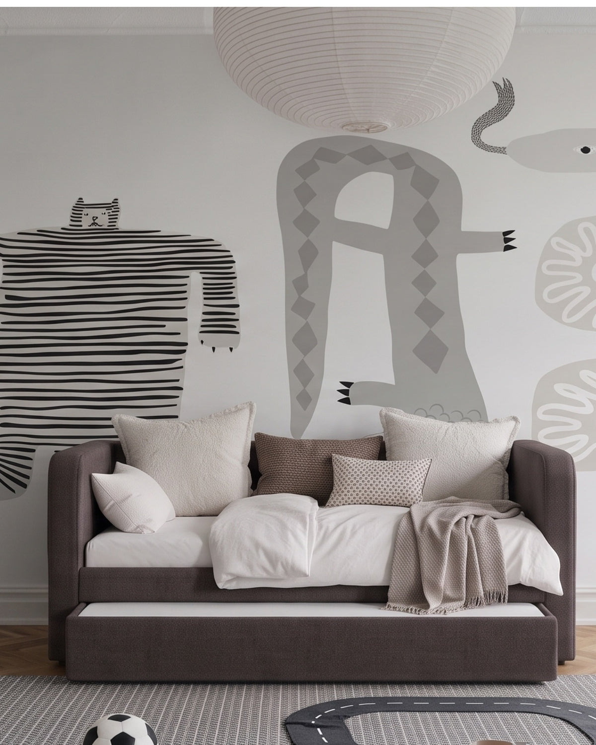 A modern children's daybed in dark brown fabric with white and beige bedding, styled in a minimalist room with a large grey animal mural on the wall and a white paper lantern hanging above. Daybed can be a bed by night, lounge by day and has an extra pull out bed for guests.