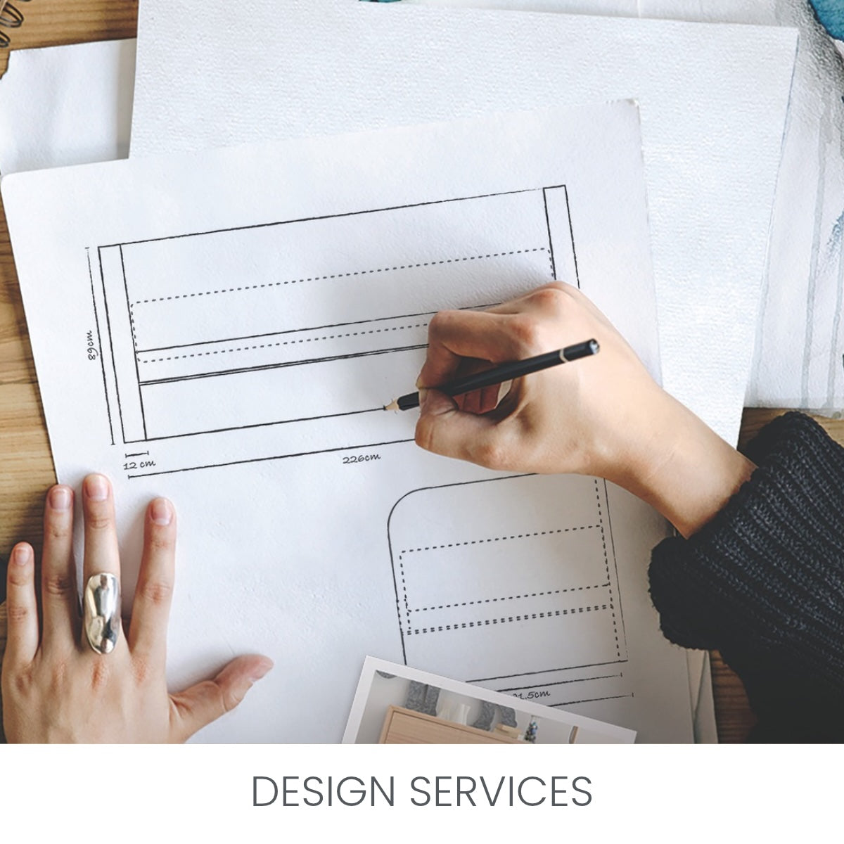 A top-down view of hands working on a design sheet with a pencil, showing a template or layout on white paper over a wooden desk. The text 'DESIGN SERVICES' appears at the bottom. Design services available for upholstered furniture products. Enquire today.