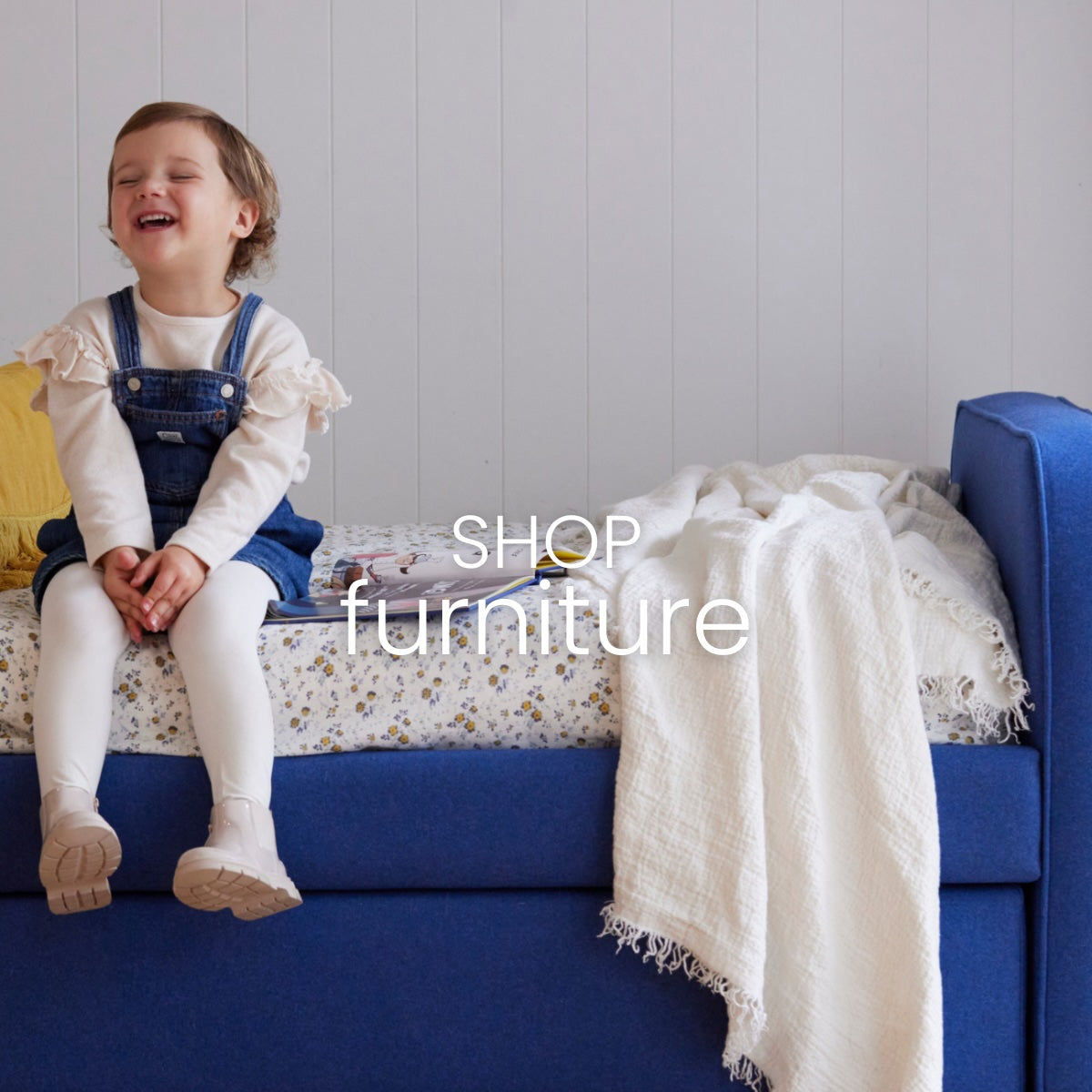 Child sitting on a blue Upholstered Bed with a white blanket, text overlay 'SHOP furniture'. Australian Made.