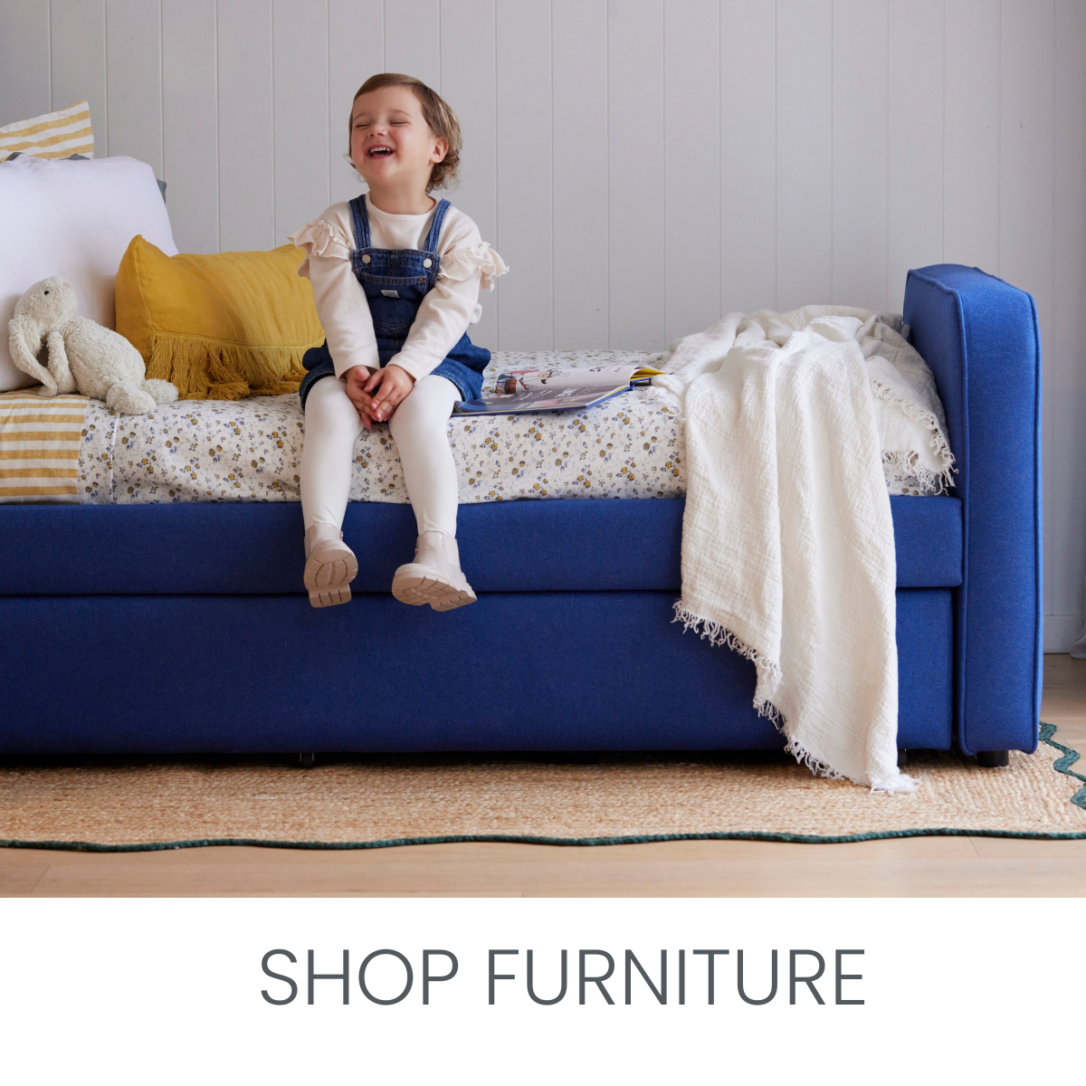Chilid sitting on a designer kid's bed. Gorgeous floral duvet and accent cushions complete the look on a cobalt blue bed.